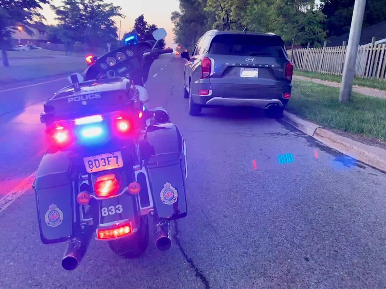 The rear-end of a Hamilton Police Service motorcycle parked on the side of the road with its lights flashing with a Hyundai SUV pulled over in front of it. 