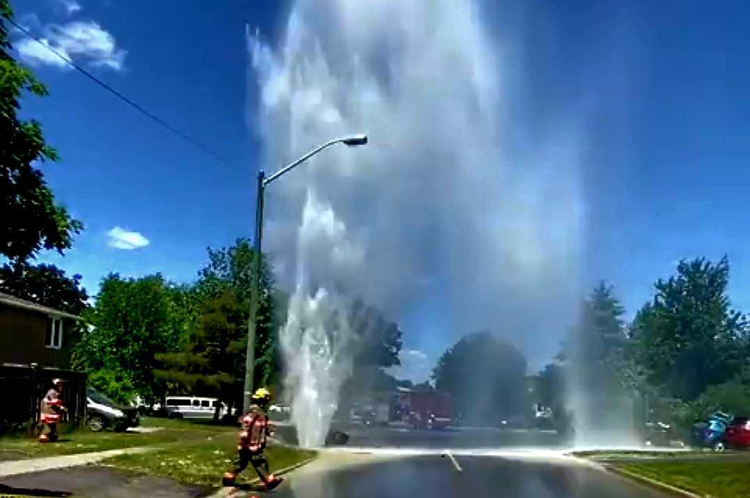 A watermain break sends a huge surge of water into the air on a residential street.